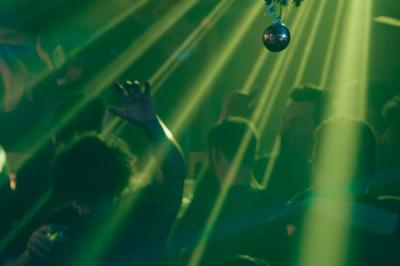 Salle animée avec des personnes dansant sous des lumières colorées, décorée de plantes suspendues et de graffitis.