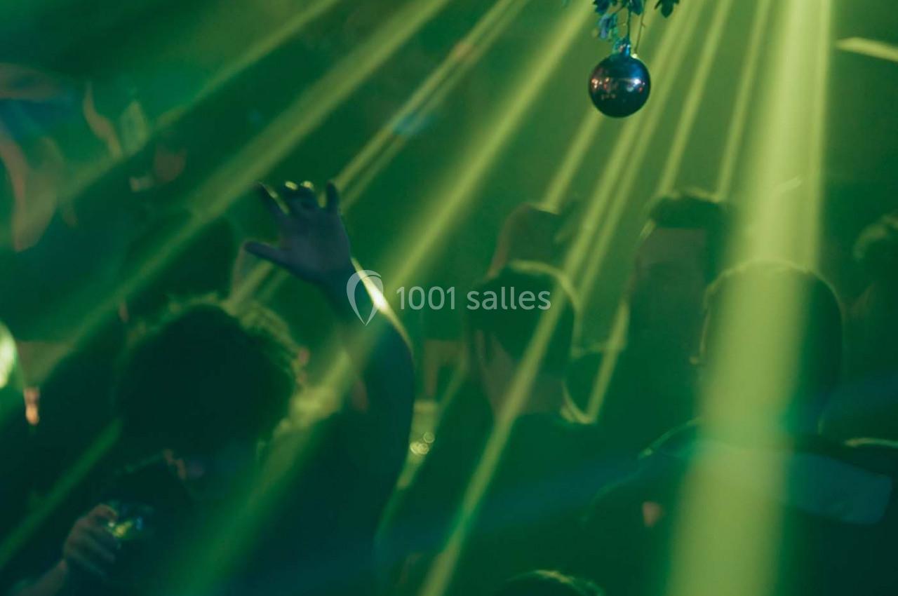 Des personnes dansent dans une ambiance sombre éclairée par des faisceaux lumineux verts et une boule disco.