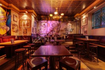 Salle de bar à la décoration punk avec murs graffités, tonneaux métalliques et mobilier en bois et velours rouge.