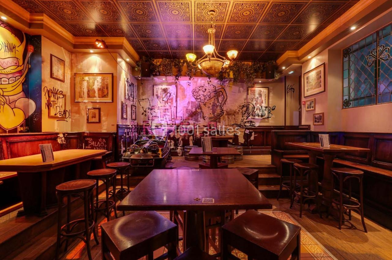 Intérieur d'un bar avec tables en bois, décorations murales artistiques et éclairage chaleureux.