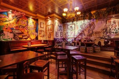 Salle de bar à la décoration punk avec murs graffités, tonneaux métalliques et mobilier en bois et velours rouge.