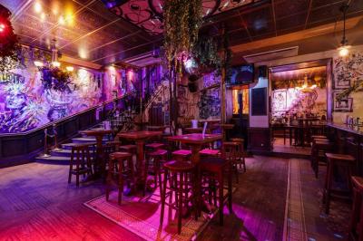 Salle de bar à la décoration punk avec murs graffités, tonneaux métalliques et mobilier en bois et velours rouge.