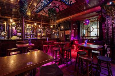 Salle de bar à la décoration punk avec murs graffités, tonneaux métalliques et mobilier en bois et velours rouge.