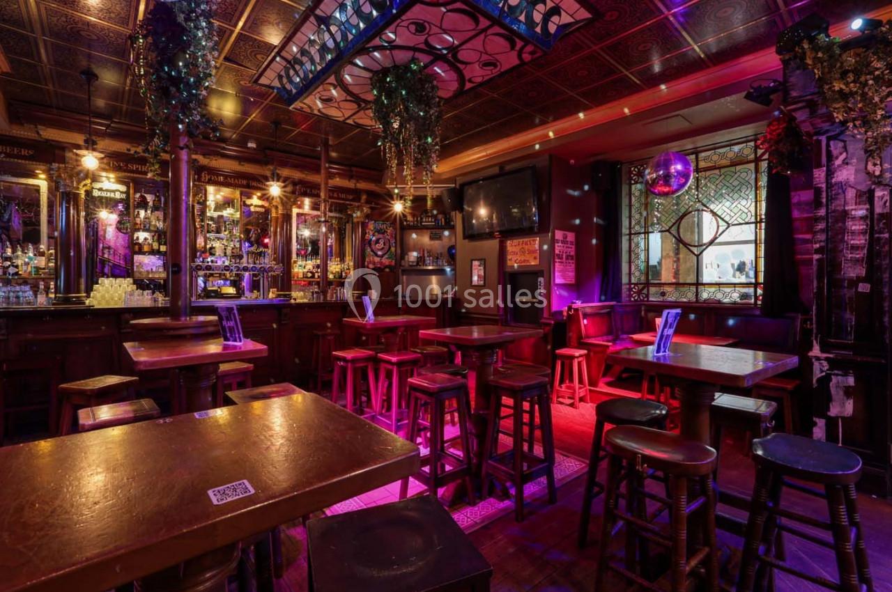Intérieur d'un bar chaleureux avec tables en bois, tabourets hauts, éclairage tamisé et décorations suspendues.