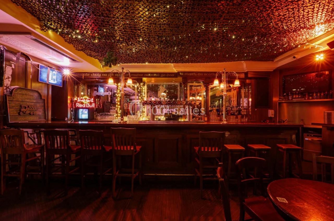 Bar en bois avec tabourets alignés, éclairage tamisé et décorations lumineuses suspendues au plafond.