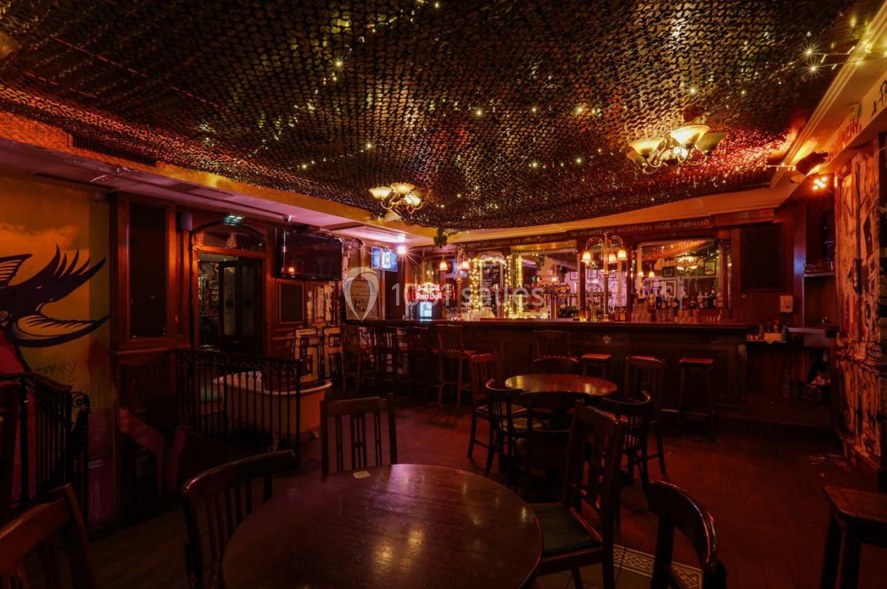 Intérieur d'un bar chaleureux avec éclairage tamisé, tables en bois et décorations lumineuses au plafond.