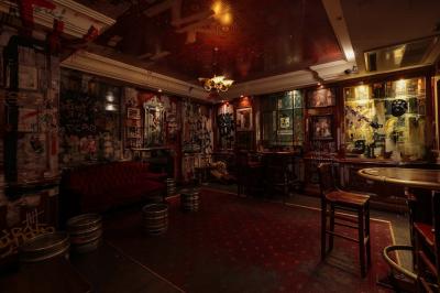 Salle de bar à la décoration punk avec murs graffités, tonneaux métalliques et mobilier en bois et velours rouge.