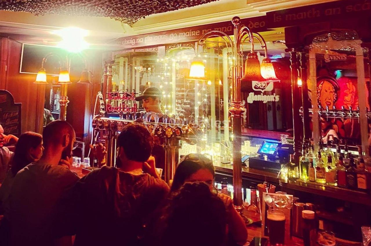 Des clients rassemblés autour d'un bar éclairé, avec un barman servant des boissons sous des lumières chaudes.