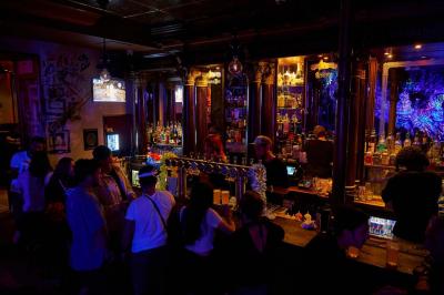 Salle de bar à la décoration punk avec murs graffités, tonneaux métalliques et mobilier en bois et velours rouge.