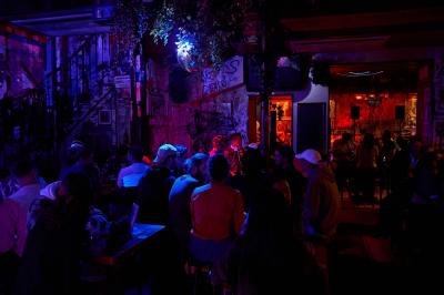 Salle de bar à la décoration punk avec murs graffités, tonneaux métalliques et mobilier en bois et velours rouge.