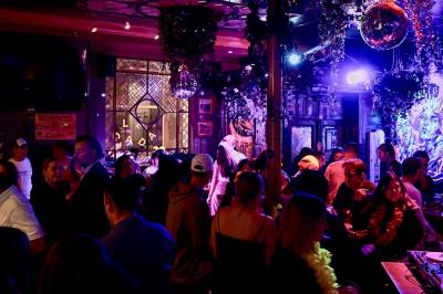Salle de bar à la décoration punk avec murs graffités, tonneaux métalliques et mobilier en bois et velours rouge.