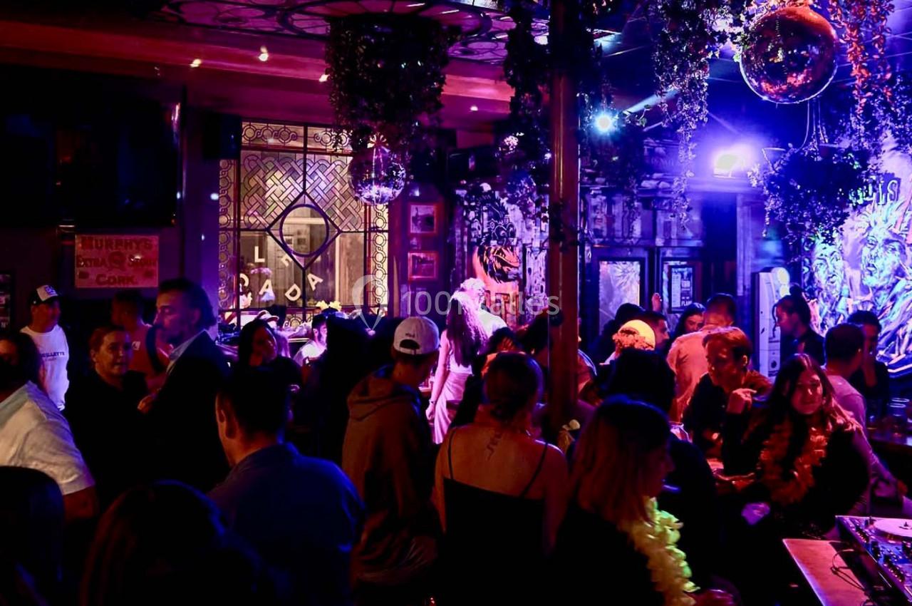 Personnes rassemblées dans un bar animé avec éclairage coloré, décorations suspendues et ambiance festive.