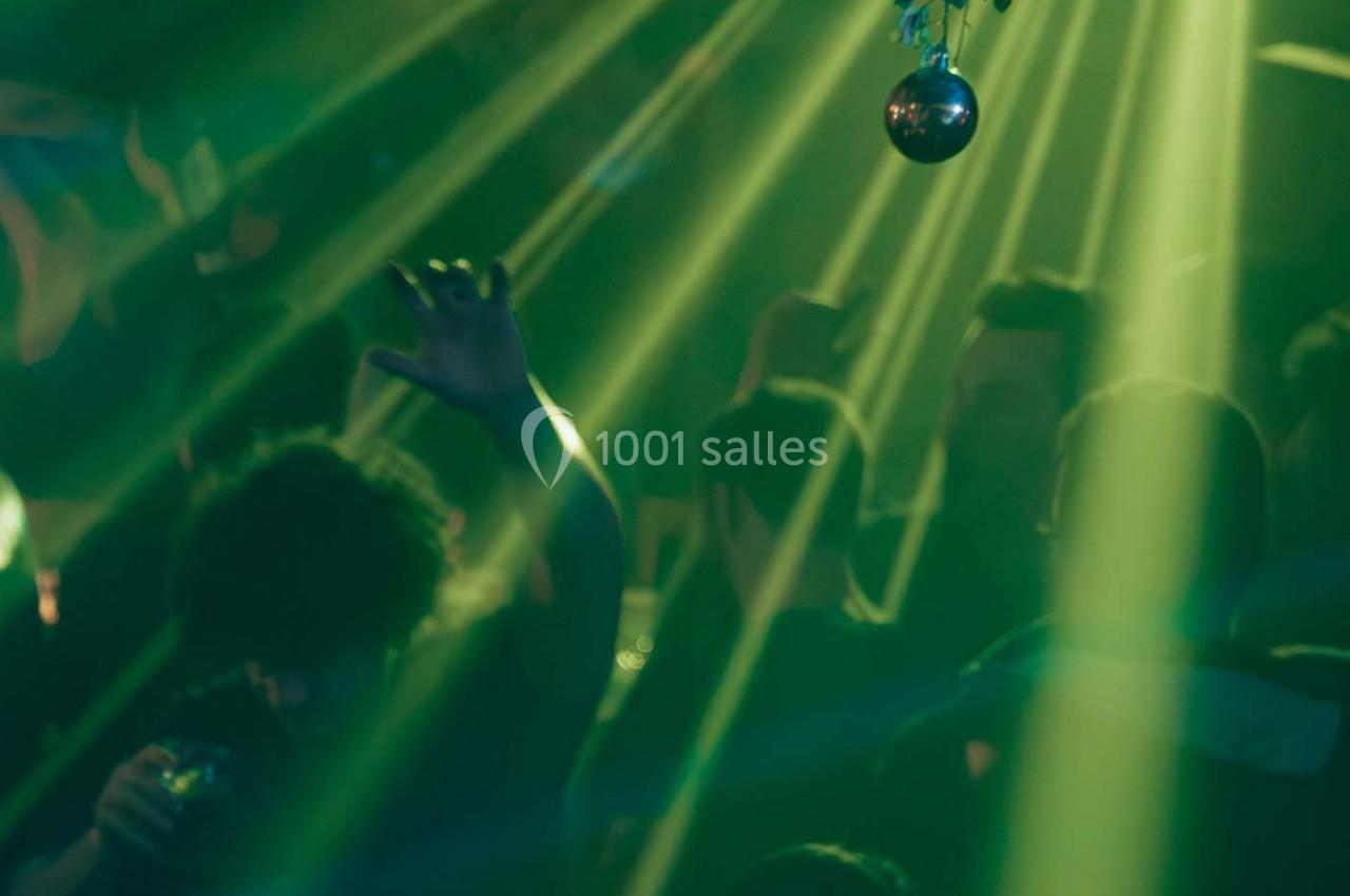 Personnes dansant sous des lumières vertes et un projecteur, avec une boule disco suspendue au plafond.