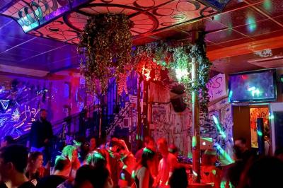 Salle de bar à la décoration punk avec murs graffités, tonneaux métalliques et mobilier en bois et velours rouge.