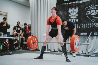 Un homme en costume bleu se tient debout sur une terrasse extérieure par temps nuageux.