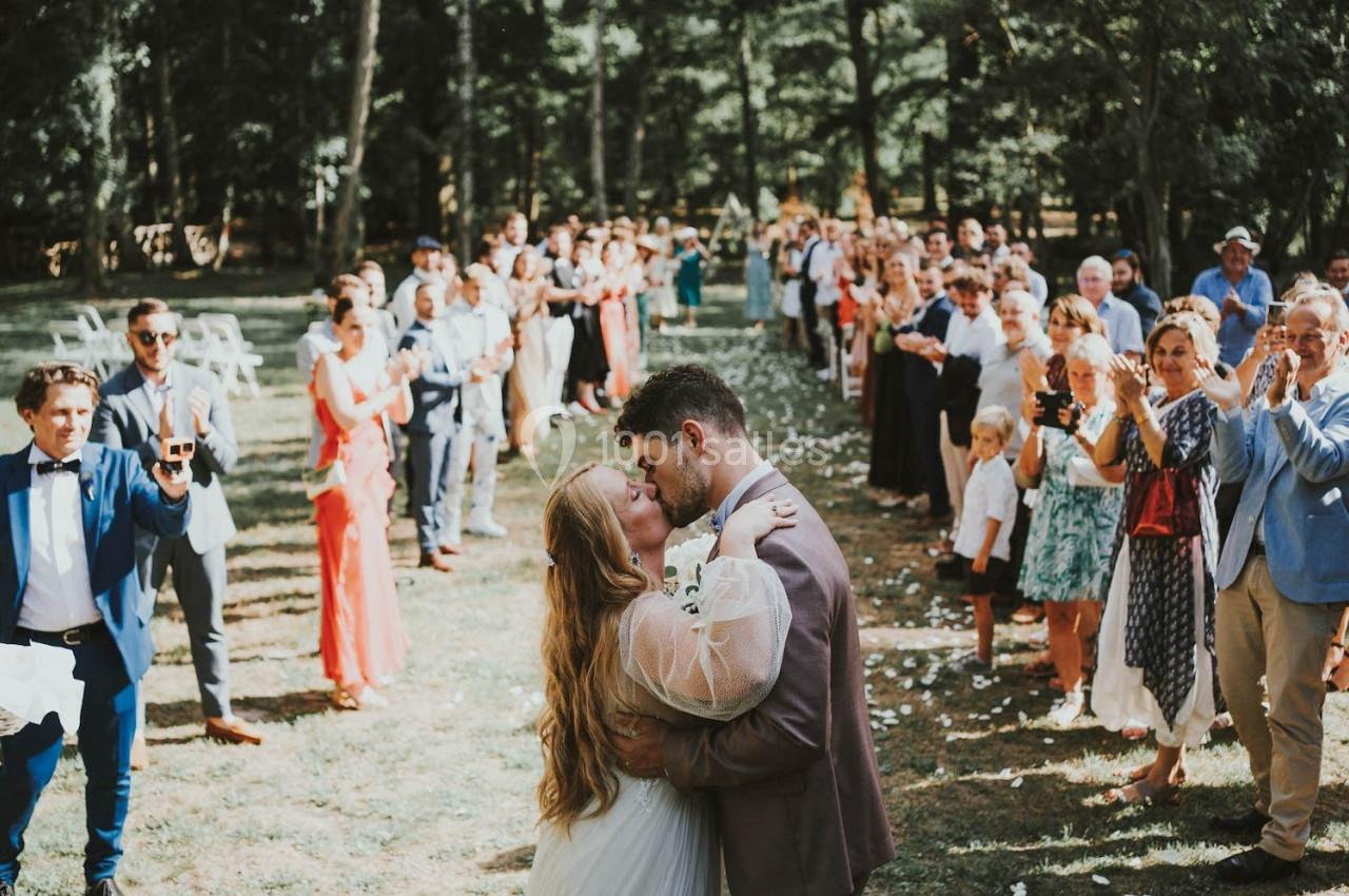 Un couple s'embrasse lors d'une cérémonie de mariage en plein air, entouré d'invités applaudissant.