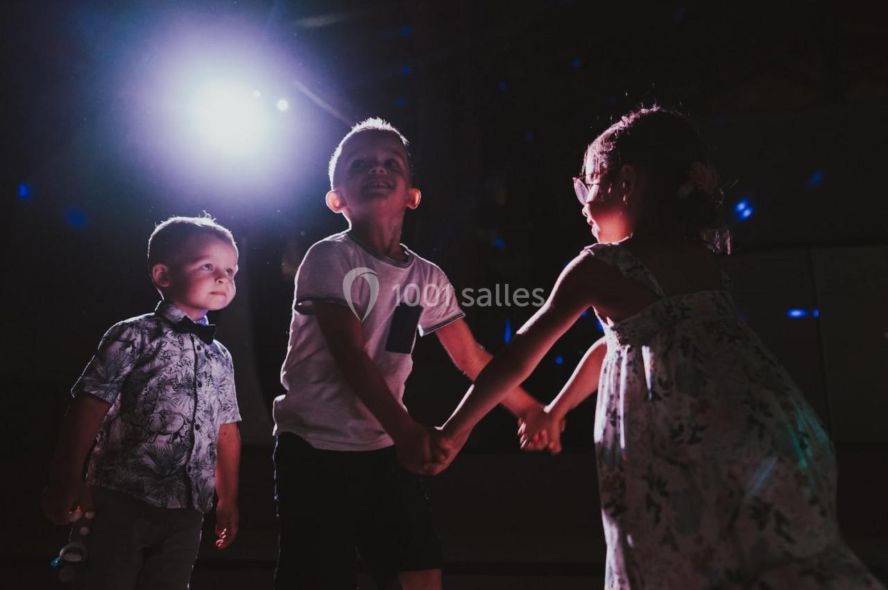 Trois jeunes enfants dansent ensemble sous une lumière vive dans un environnement sombre.