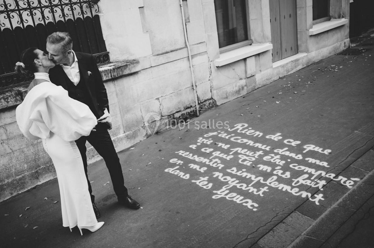 Un couple s'embrasse tendrement sur un trottoir, près d'un texte manuscrit peint au sol.