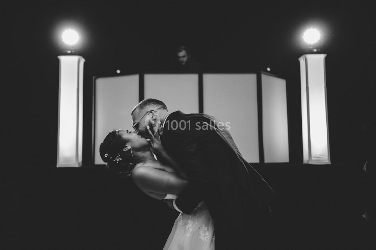 Un couple s'embrasse lors d'une danse de mariage, éclairé par des lumières de scène en arrière-plan.