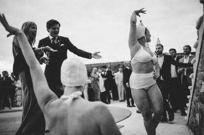 Des personnes en tenue élégante regardent des danseuses en maillot de bain et bonnet, lors d'un événement en extérieur.