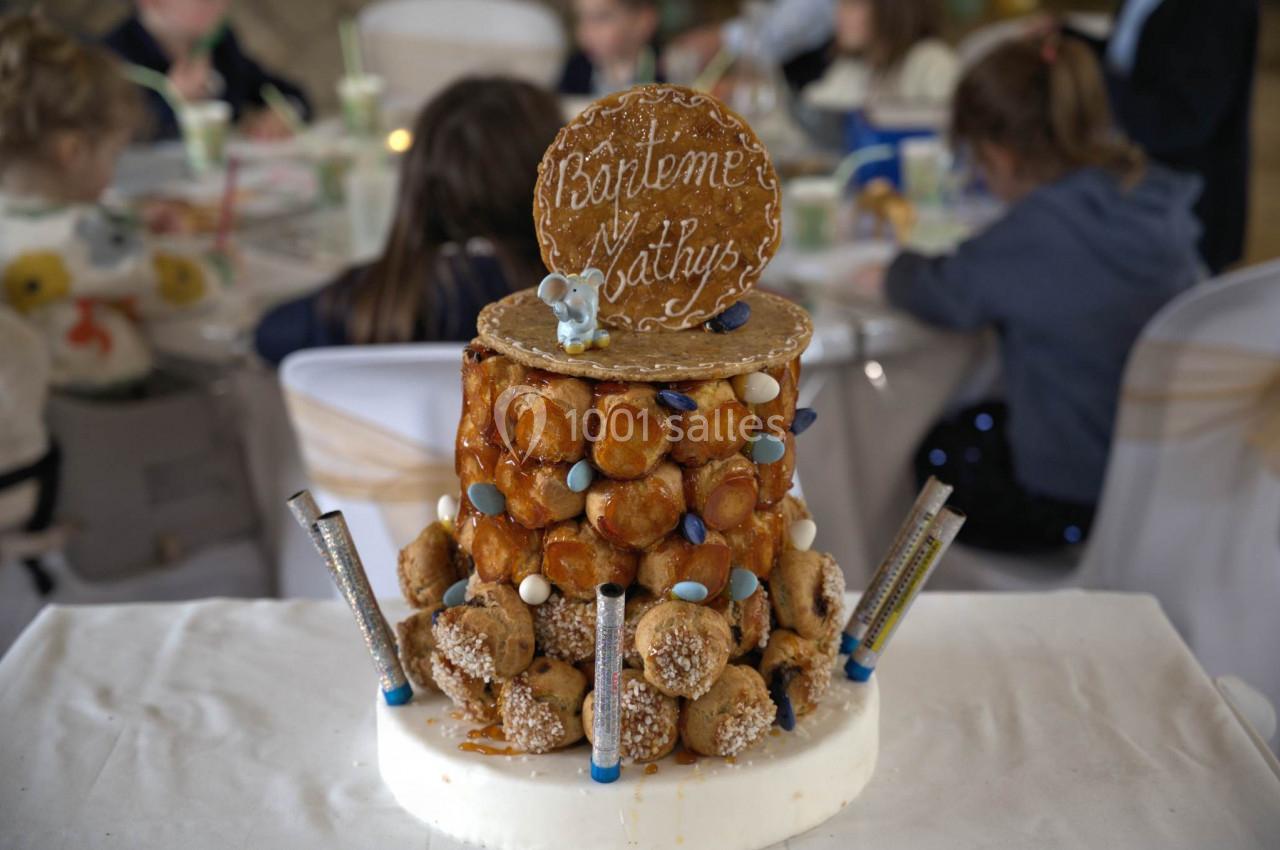 Pièce montée en choux décorée pour un baptême, avec un disque en sucre portant une inscription et des décorations colorées.