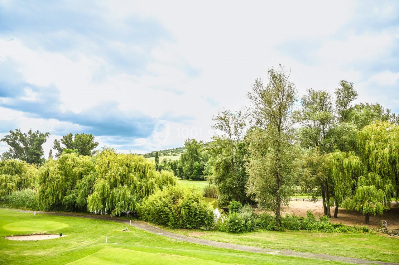 Paysage verdoyant avec des arbres, un terrain de golf et un ciel partiellement nuageux en arrière-plan.