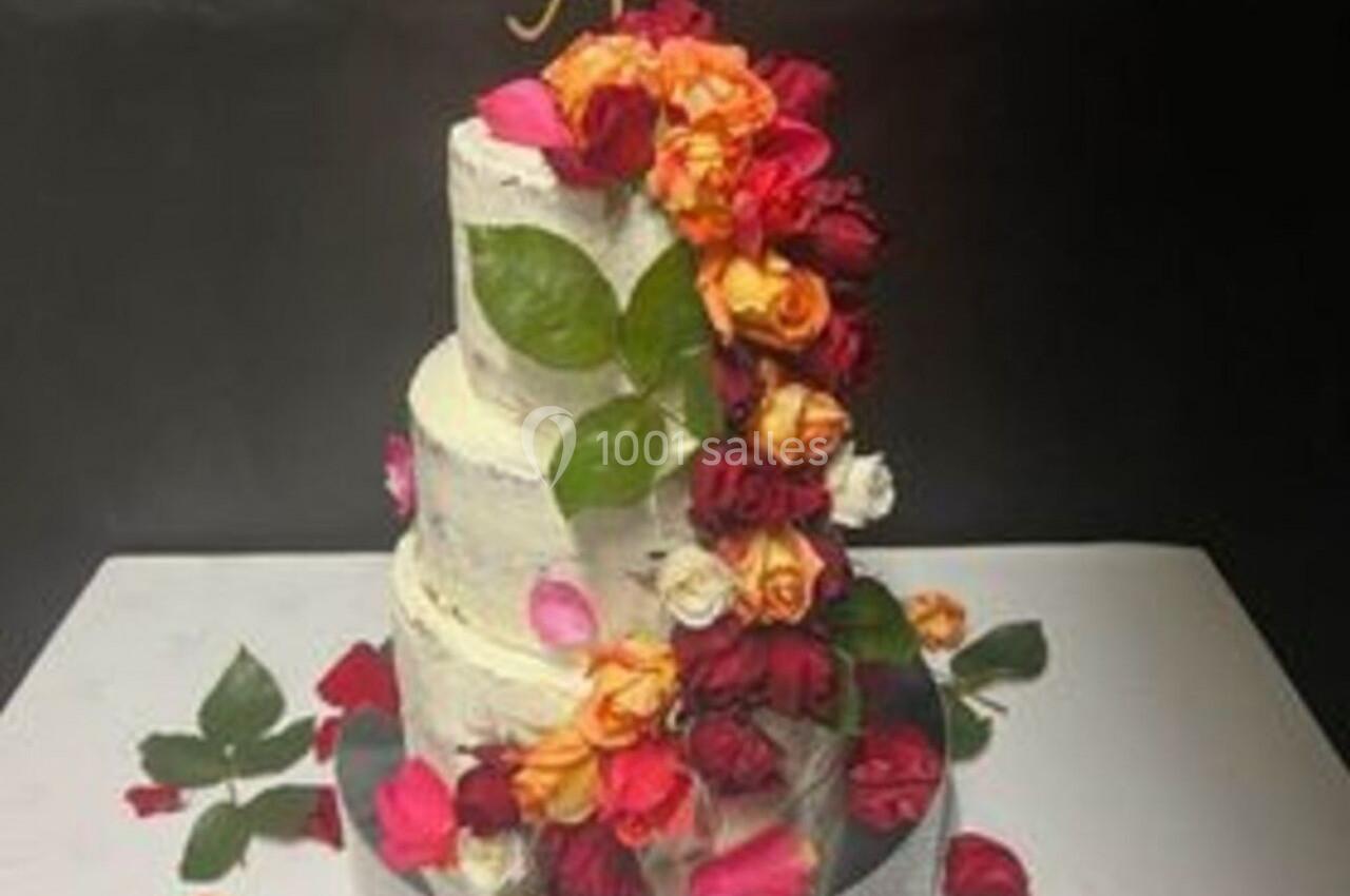 Gâteau de mariage à trois étages décoré de roses colorées et de feuilles, sur fond noir.