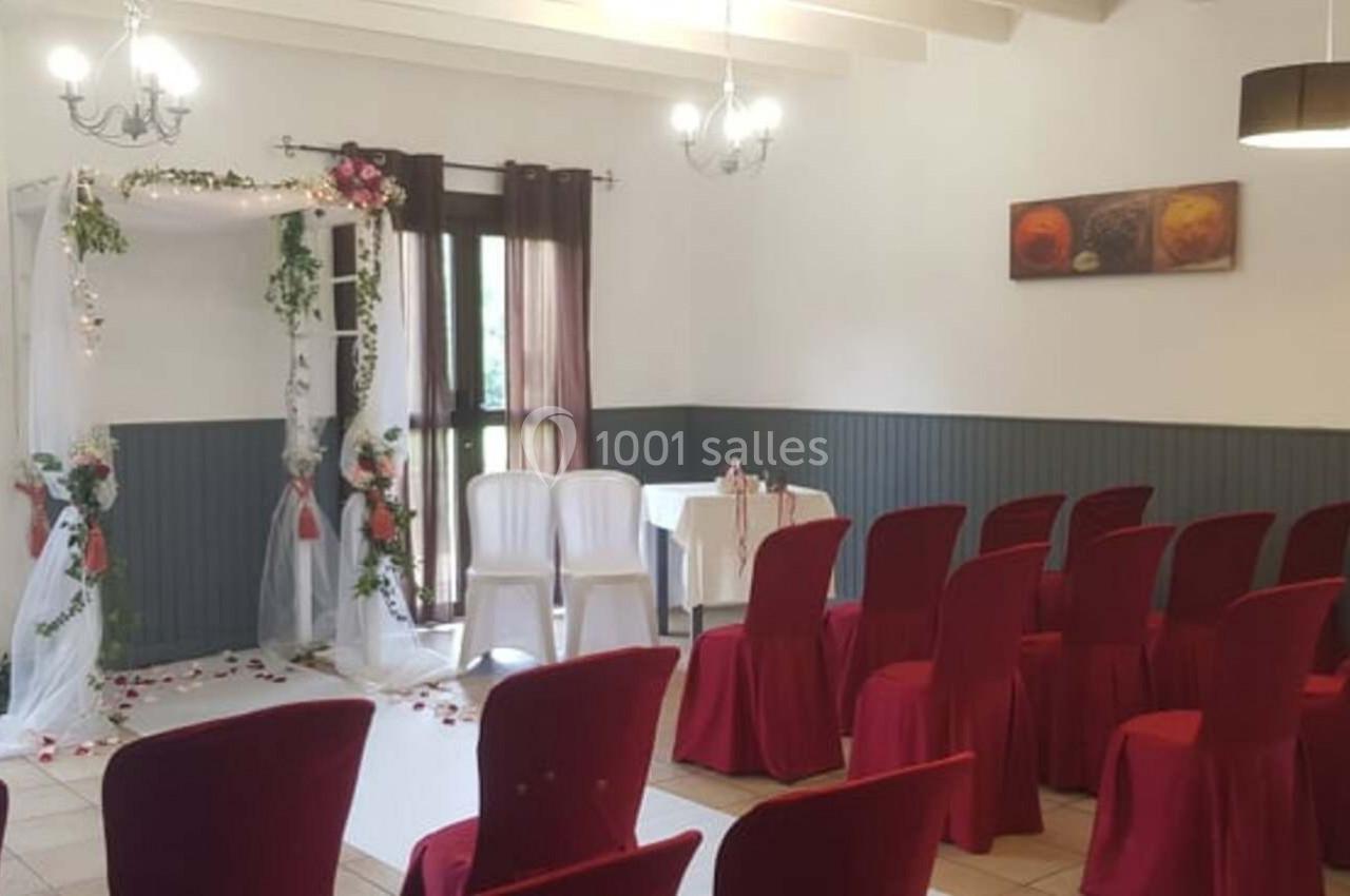 Salle décorée pour une cérémonie, avec une arche fleurie, des chaises rouges et un éclairage suspendu.