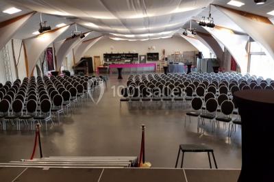 Salle de réception aménagée avec des tables dressées pour un événement, éclairage tamisé et scène en arrière-plan.