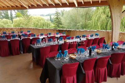 Salle de réception aménagée avec des tables dressées pour un événement, éclairage tamisé et scène en arrière-plan.