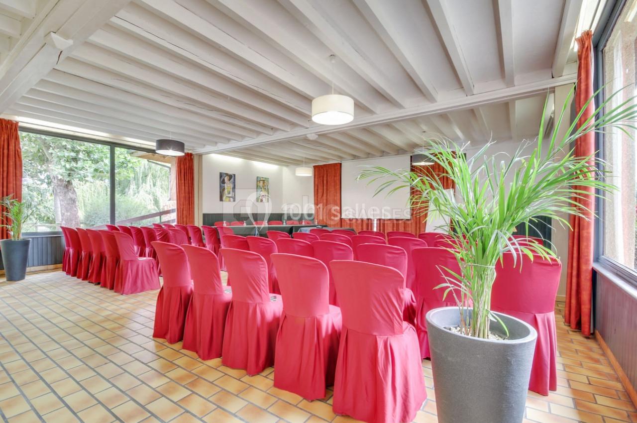 Salle de réunion lumineuse avec des chaises rouges alignées, grandes fenêtres et plantes en pot.