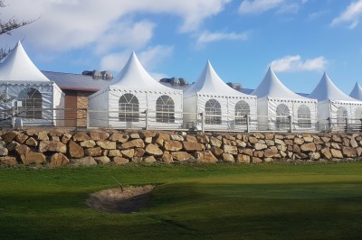 Salle de réception aménagée avec des tables dressées pour un événement, éclairage tamisé et scène en arrière-plan.