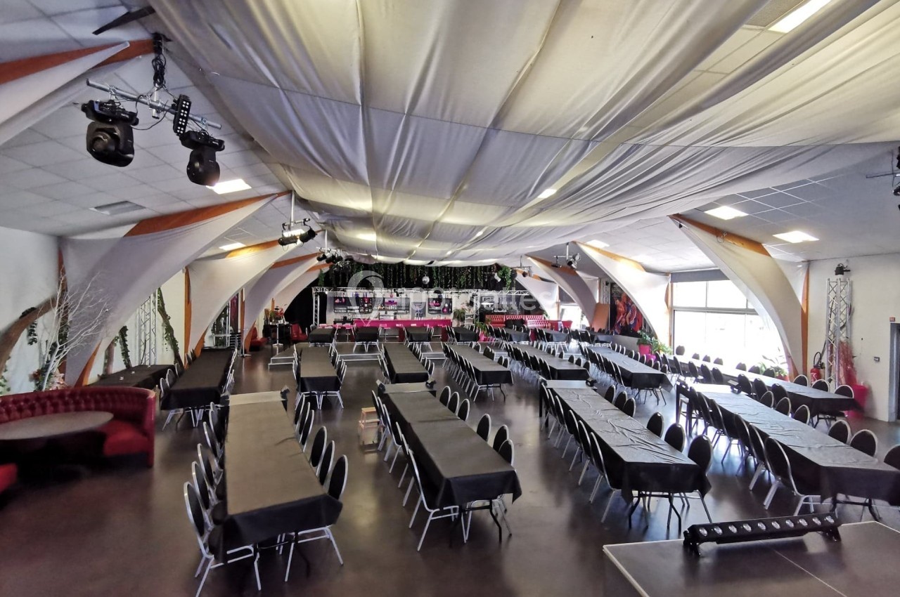 Salle de réception spacieuse avec tables rectangulaires dressées de nappes noires, éclairage naturel et décorations…