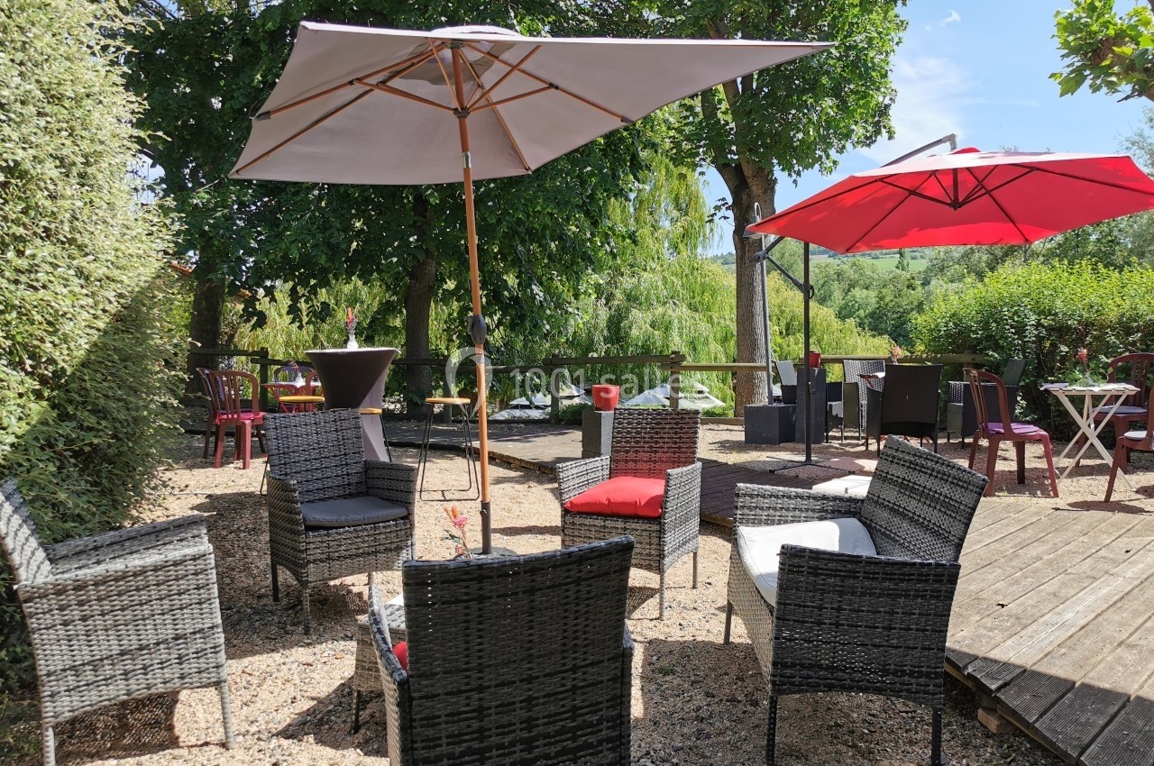 Mobilier de jardin en rotin avec parasols sur une terrasse extérieure entourée de verdure.