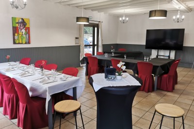 Salle de réception aménagée avec des tables dressées pour un événement, éclairage tamisé et scène en arrière-plan.