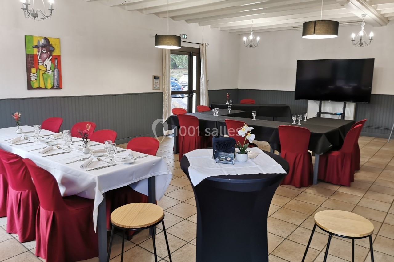 Salle lumineuse aménagée pour un événement, avec tables dressées, chaises rouges et décoration sobre.