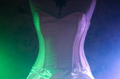 Corset blanc en dentelle et satin éclairé par des lumières vertes et violettes dans un environnement sombre.