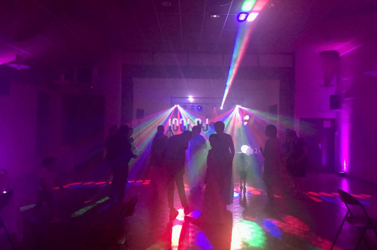 Personnes dansant dans une salle sombre éclairée par des lumières colorées et des faisceaux laser.