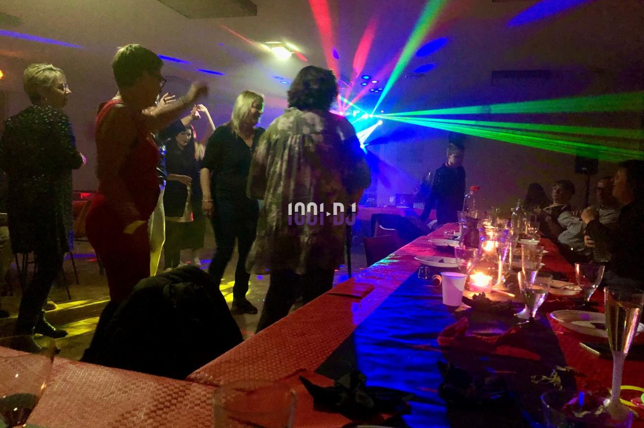 Des personnes dansent sous des lumières colorées dans une salle décorée avec des tables dressées.