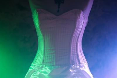 Corset blanc en satin et dentelle, éclairé par des lumières colorées dans un environnement sombre.