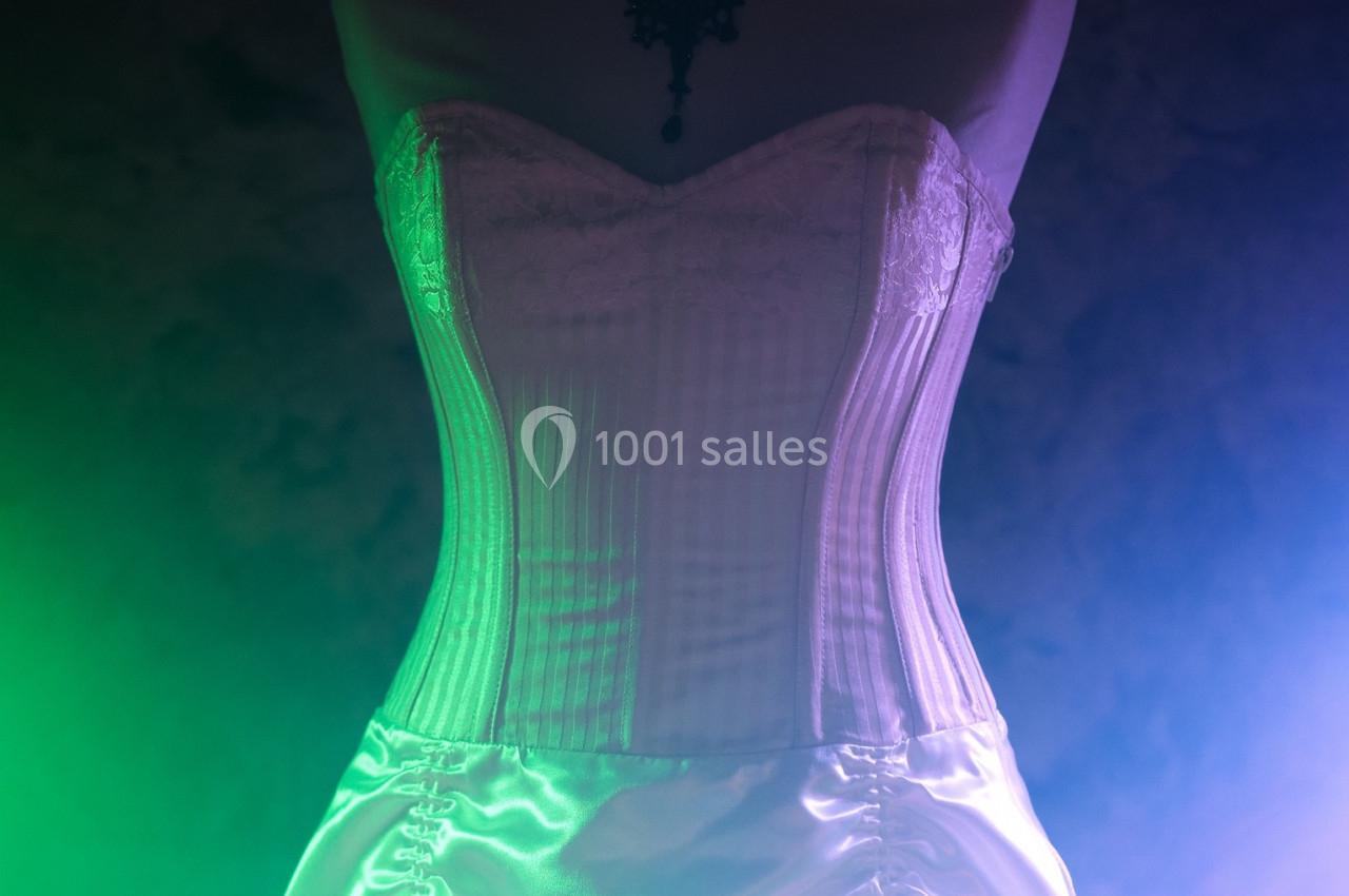 Corset blanc en satin et dentelle, éclairé par des lumières colorées dans un environnement sombre.