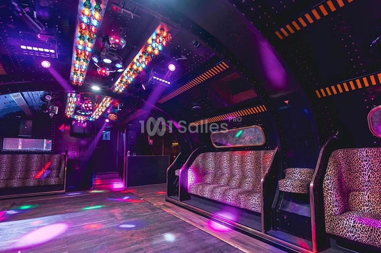 Intérieur d'une salle de fête avec banquettes léopard, éclairages colorés et piste de danse en bois.