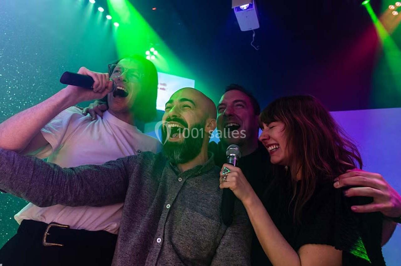 Quatre personnes chantent ensemble au karaoké sous des lumières colorées, souriantes et enthousiastes.