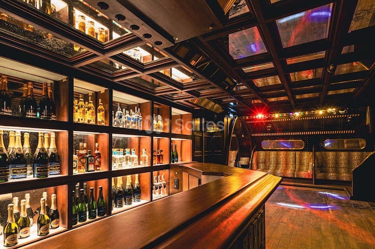 Intérieur d'un bar avec des étagères illuminées contenant des bouteilles et un espace lounge en arrière-plan.