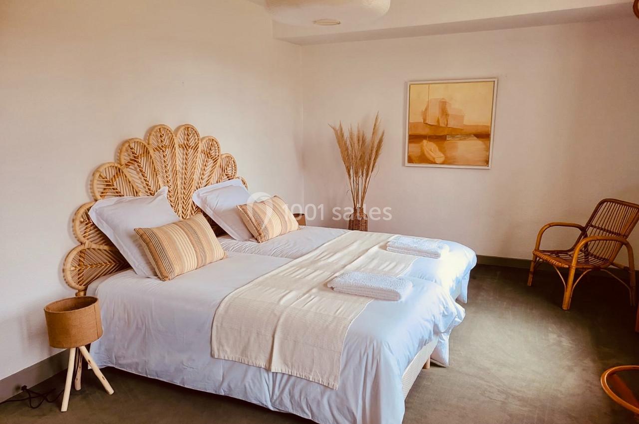 Chambre lumineuse avec lits jumeaux, tête de lit en rotin, décoration minimaliste et chaise en bois.