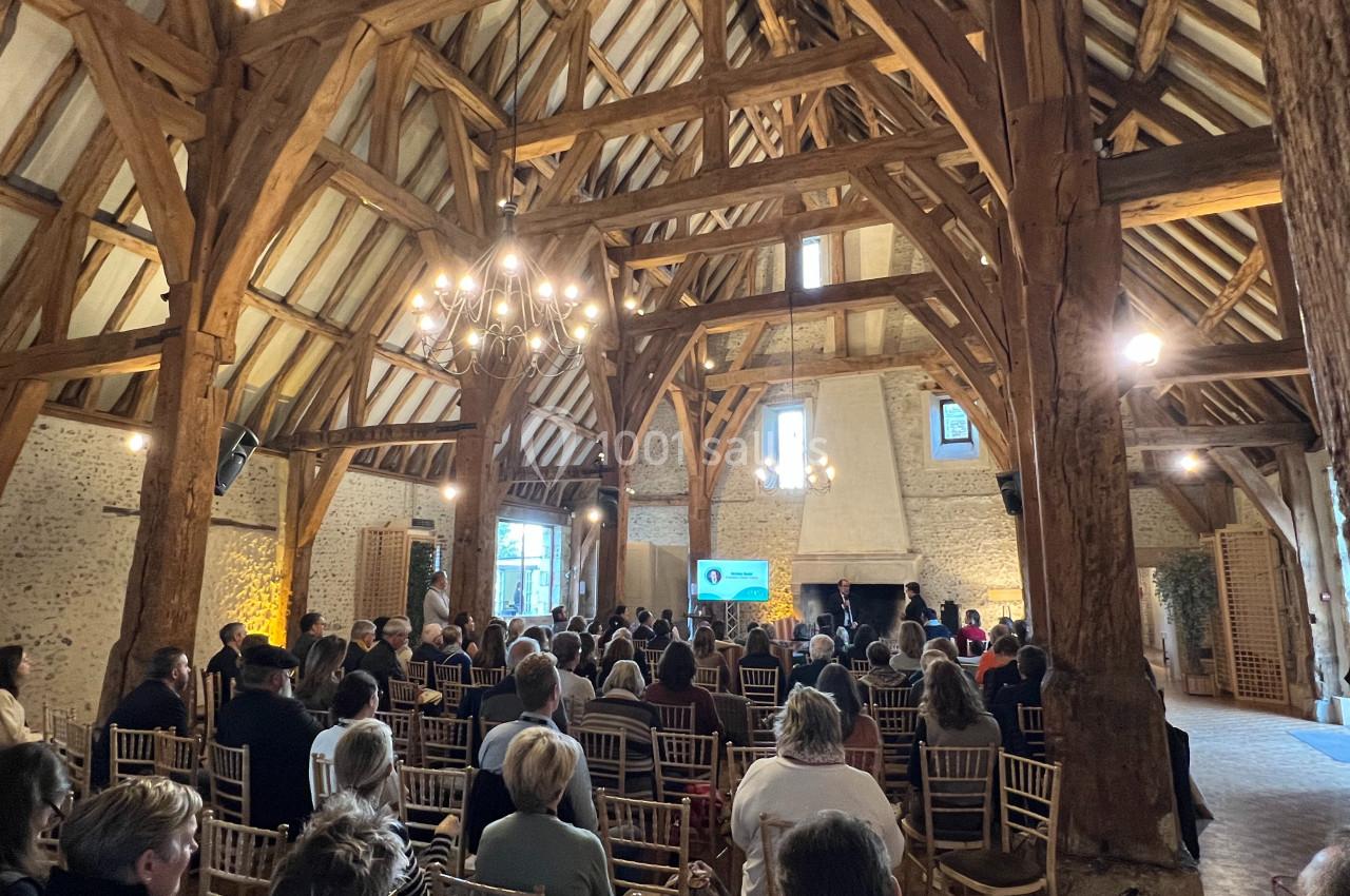 Salle en bois avec poutres apparentes, public assis face à un écran lors d'une présentation ou conférence.