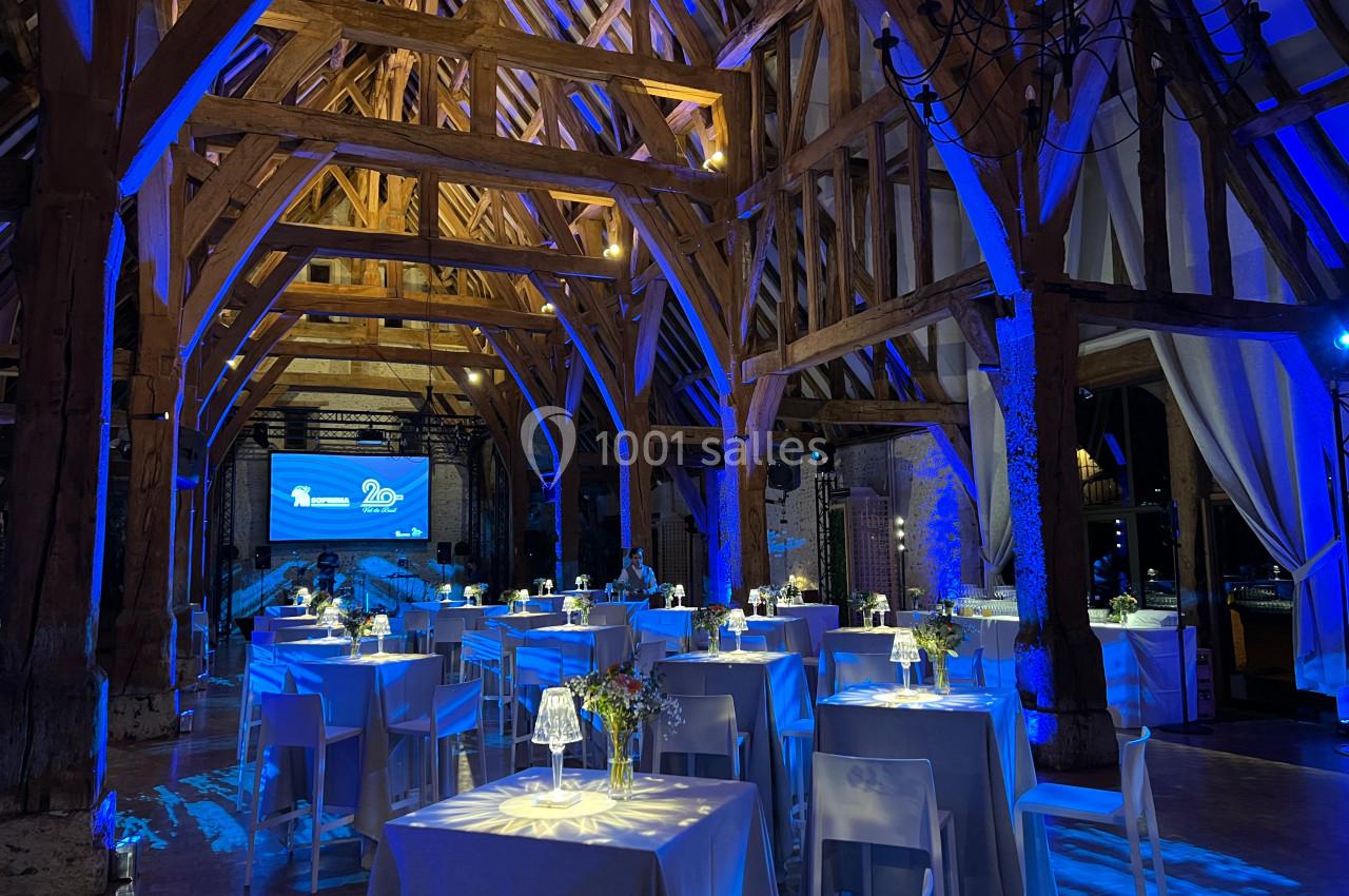 Salle de réception en bois avec tables décorées et éclairage bleu, écran de projection en arrière-plan.