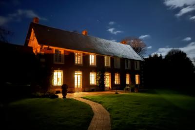 Salon lumineux avec poutres apparentes, canapé blanc, table basse en bois, lampes allumées et vue sur jardin.