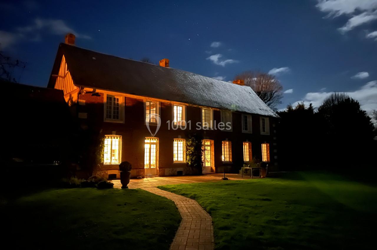 Maison en briques éclairée de nuit, entourée d'un jardin avec une allée pavée menant à l'entrée.