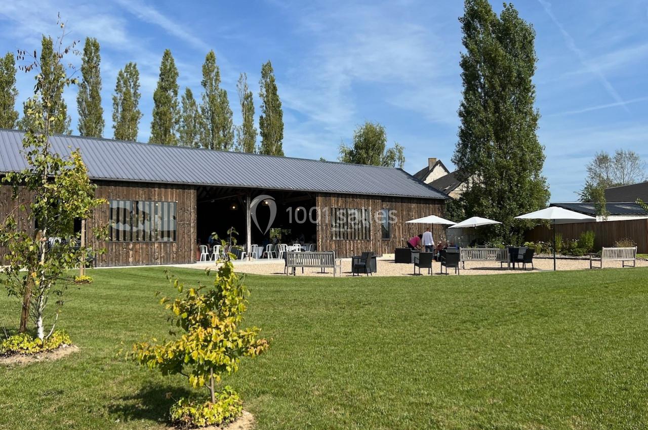 Bâtiment en bois avec terrasse aménagée, parasols et espaces verts sous un ciel dégagé.